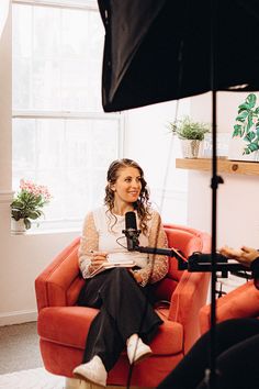 a woman sitting in an orange chair with a microphone and another person standing behind her