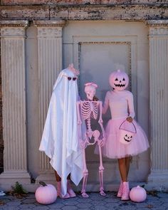 two people in costumes standing next to each other with pumpkins on the ground behind them