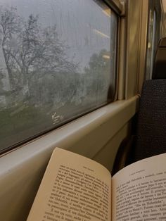 an open book sitting on top of a seat next to a window with trees outside