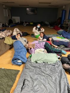 group of people laying on the floor with sleeping bags and blankets around them in an open room