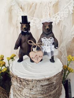 two brown bears standing on top of a wooden stump with a wedding cake decoration in the shape of a heart