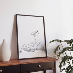 an open book is on a table next to a plant and a vase with a bird in it