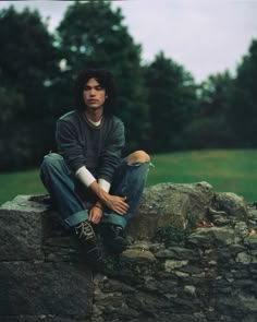 a young man sitting on top of a stone wall next to a lush green field