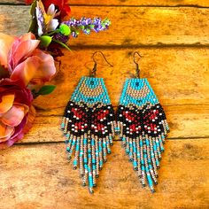 a pair of blue and red beaded earrings next to flowers on a wooden surface