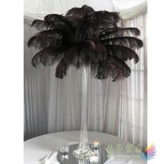 an ostrich feather centerpiece in a tall glass vase on a round table