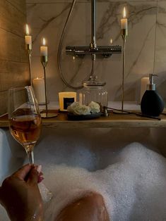 a person is taking a bath with wine in the tub and candles on the wall