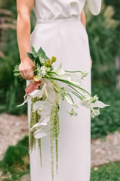 a woman in a white dress holding a bouquet of flowers and greenery on her wedding day