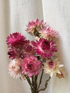 a vase filled with lots of pink flowers on top of a white cloth covered table