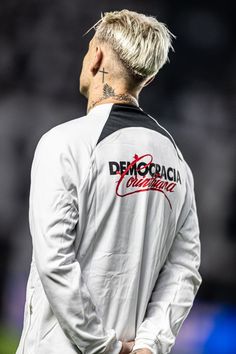 a man with white hair and tattoos on his face standing in front of a soccer field