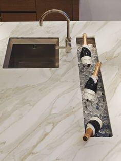 two bottles of wine sitting on top of a marble countertop next to a sink