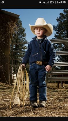 a young boy wearing a cowboy hat and holding a lasso in his hand while standing on the ground