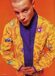 a man with his hands on his hips wearing a yellow and purple jacket, looking at the camera