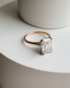 a gold ring with an emerald cut diamond on it sitting on top of a white table