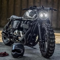 a black motorcycle parked next to a helmet on the ground with it's lights on