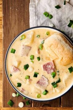 a bowl filled with soup on top of a wooden table next to bread and green onions