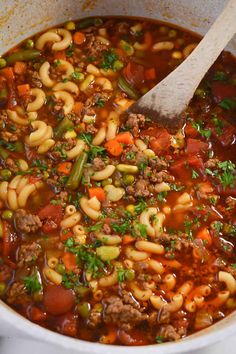 a large pot filled with pasta and meat soup next to a wooden spoon in it