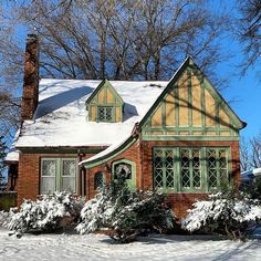 a house with snow on the roof and bushes in front of it, surrounded by trees