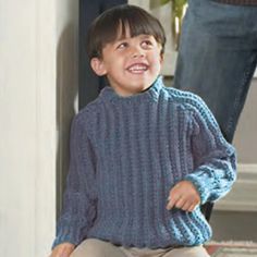 a young boy sitting on the floor wearing a blue sweater