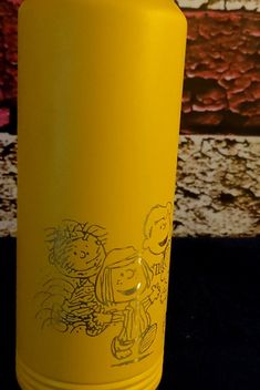 a yellow water bottle sitting on top of a black table next to a wall with pictures