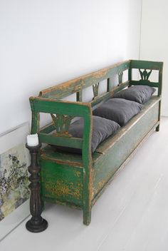 an old green bench with pillows on it and a candle in the corner next to it