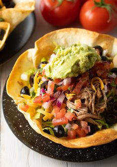 a black plate topped with nachos and guacamole next to tomatoes