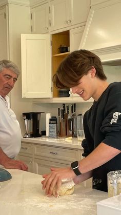 an older man and young woman preparing food in a kitchen with white cabinets, counter tops and appliances