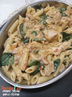 pasta with chicken, spinach and sauce in a silver bowl on a black plate