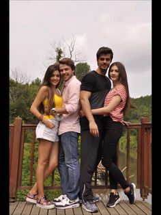 a group of young people standing next to each other on a wooden deck with trees in the background