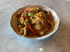 a bowl filled with noodles and meat on top of a marble countertop next to a bottle