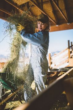 a woman in overalls is holding hay