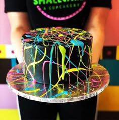 a person holding a cake decorated with multicolored icing