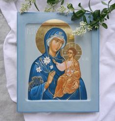 an icon of the virgin mary and child jesus on a blue frame with flowers in front of it