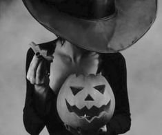 a woman wearing a hat and holding a jack - o'- lantern in front of her face