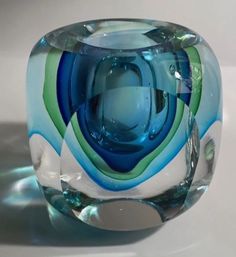 a blue and green glass vase sitting on top of a white tableclothed surface