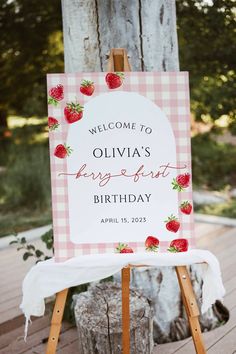 a welcome sign with strawberries on it sitting on a wooden easel in front of a tree