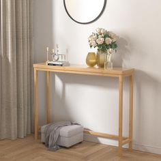 a wooden table with a mirror and vase on it in front of a white wall