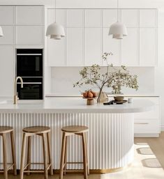 a white kitchen with three stools next to an island