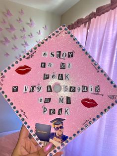 a person holding up a pink graduation cap with photos on it and words written in different languages