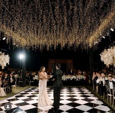 a bride and groom standing on a checkered floor in front of an audience at their wedding reception