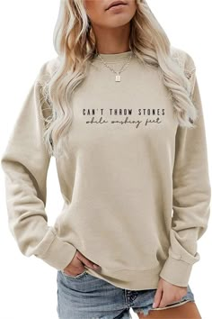 a woman wearing a tan sweatshirt with the words can't throw stones on it