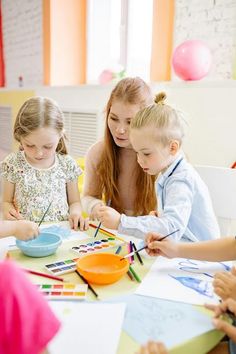 a group of children sitting around a table with paper and colored pencils