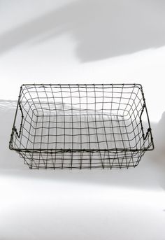 a wire basket with white sheets in it on a white surface, next to a shadow from the wall