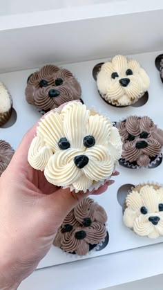 a person holding a cupcake with icing in the shape of a dog's face