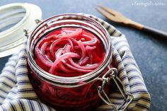 a jar filled with red pickles sitting on top of a table next to scissors