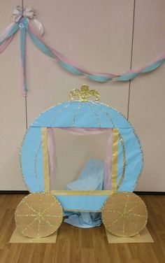 a blue and gold carriage made out of cardboard on the floor with ribbons around it