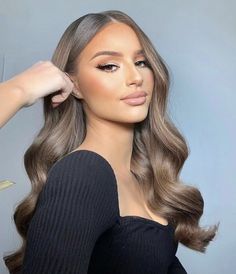 a woman with long, wavy hair is wearing a black top and has her hand on her head