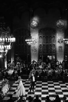 black and white photo of bride and groom dancing on checkerboard floor in ballroom