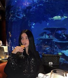 a woman sitting at a table with a wine glass in her hand and an aquarium behind her