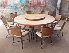 a wooden table surrounded by wicker chairs in front of a wall with graffiti on it