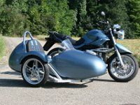 a silver motorcycle parked on the side of a road next to a lush green forest